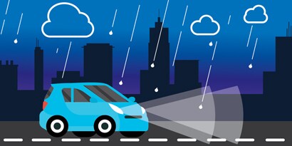 A graphic of a blue car in the rain at night, with its headlights illuminating the road markings ahead.
