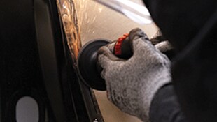 A gloved hand using a handheld abrasive tool on a metal surface
