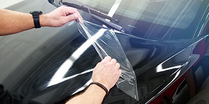 person putting a clear plastic wrap on a car
