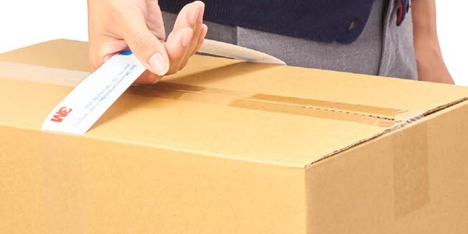 A close up of a person's hand holding a cardboard box with a 3M carry handle
