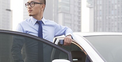 A professional-looking man stands behind an open car door, showing how the window tint creates a soft gray hue.
