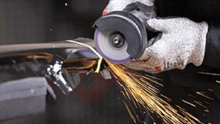 A gloved hand operating a rotary grinding tool on metal
