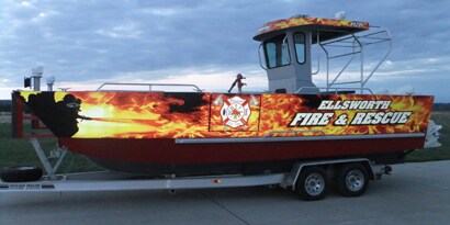 A boat on a trailer reflects light off its boat wrap that has images of flames.
