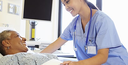 Healing sunlight streams through the window as a female nurse in blue scrubs tends to a patient.

