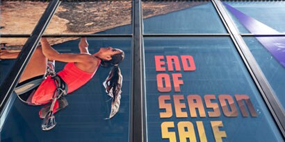 A large-scale window graphic shows a woman rock-climbing and the words “end of season sale.