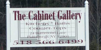 A big white sign wrapped in 3M colored films that says The Cabinet Gallery and phone number in maroon font.
