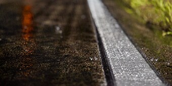 A close-up photo shows a wet road and a highly visible road marking.
