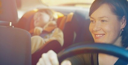 A mom glances in the rearview mirror of her car to see her baby sleeping contentedly beneath a sunny window protected by automotive window tinting.
