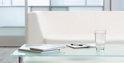 3MTM Glass Finishes cover windows in a hotel lobby where a white couch and newspapers invite travelers to rest.
