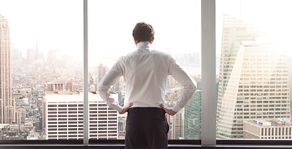 A man stands with his back to the camera, hands on his hips. He looks out sunny office building windows that are covered with 3M™ Sun Control Window Film.
