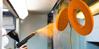 A person in PPE powder-coating two disc- shaped equipment
