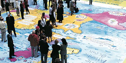 Dozens of people gather on a vivid floor wrap of a world map.

