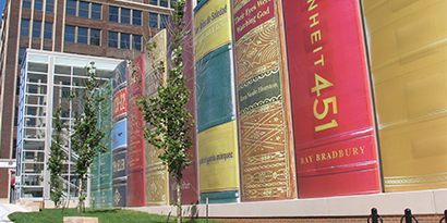 A building exterior has a large-scale graphic wrap featuring the spines of books.
