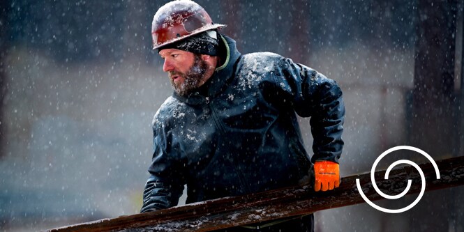 Image of a construction worker carrying materials through a steady snowfall
