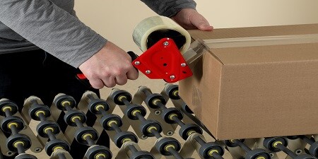A person seals a cardboard box with packing tape using a tape dispenser.
